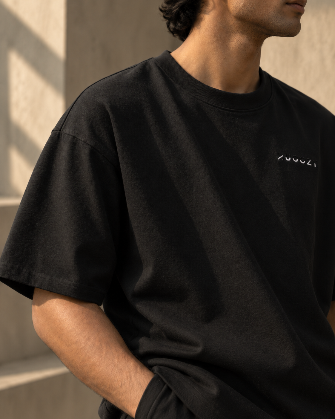 HUGGZY oversized black T-shirt in warm daylight, close editorial detail of the cotton and shoulder seam